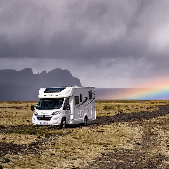 Wohnmobil in weiter Landschaft mit Regenbogen im Hintergrund.